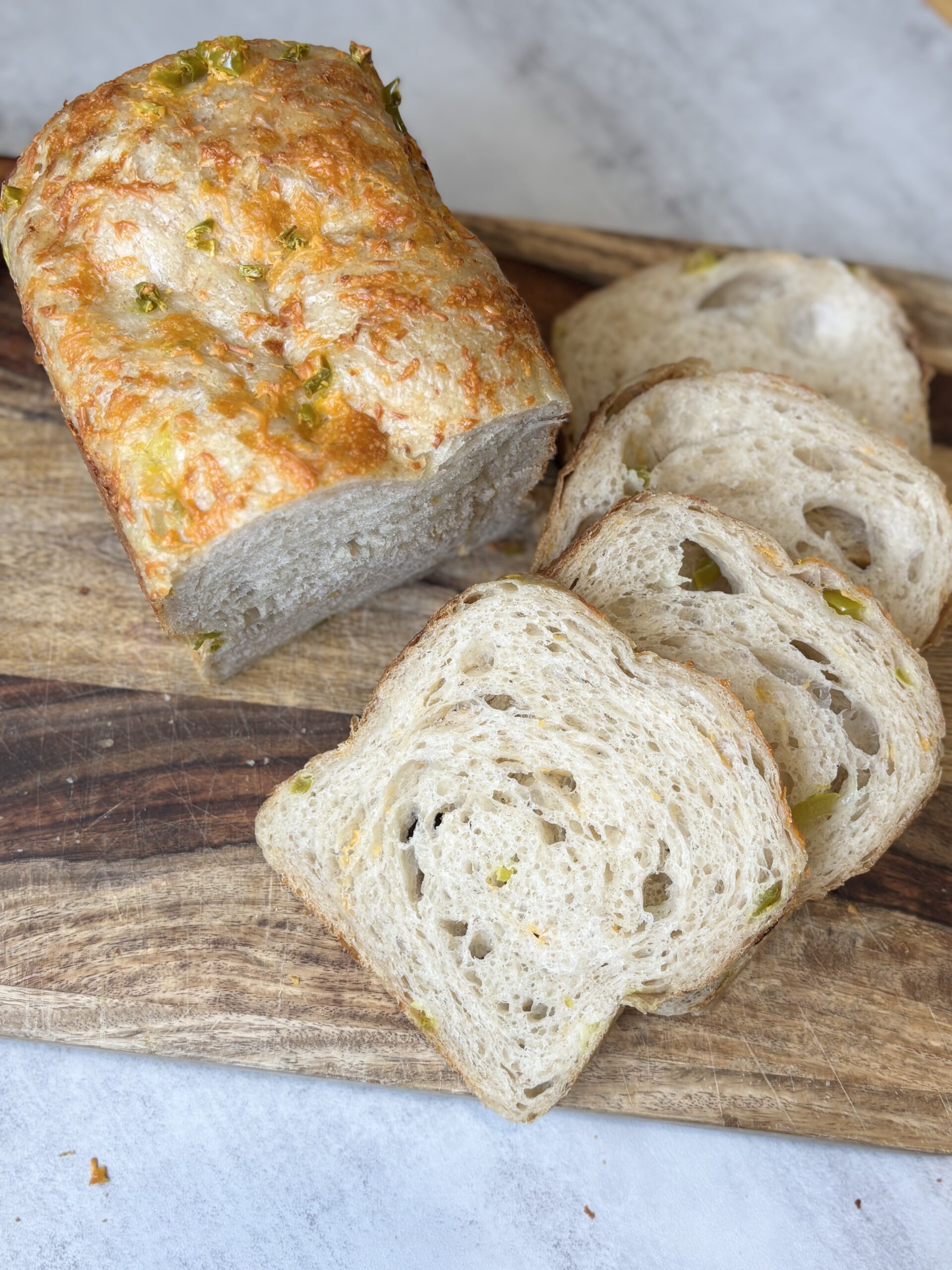 sliced up Hot Honey Cheddar Jalapeño Sourdough bread on a wood cutting board.