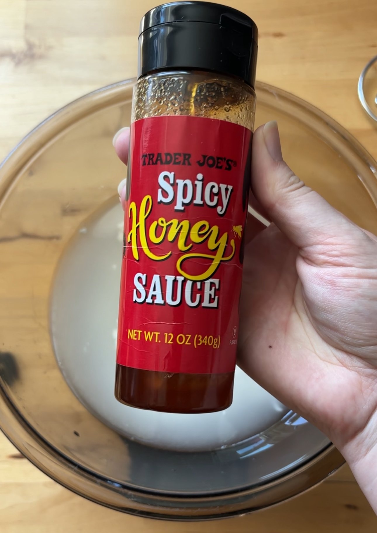 A hand holding a bottle of trader joes spicy honey sauce
