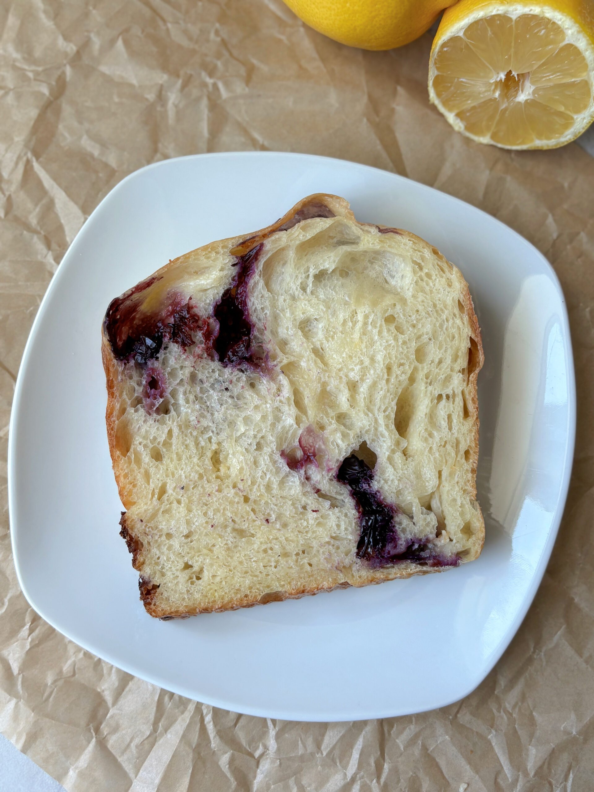 a sliced piece of Lemon Blueberry Sourdough on a white plate with lemons on the side.
