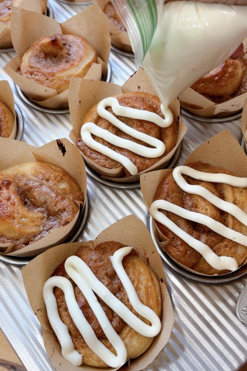 putting icing on sourdough protein cinnamon rolls in a muffin tin