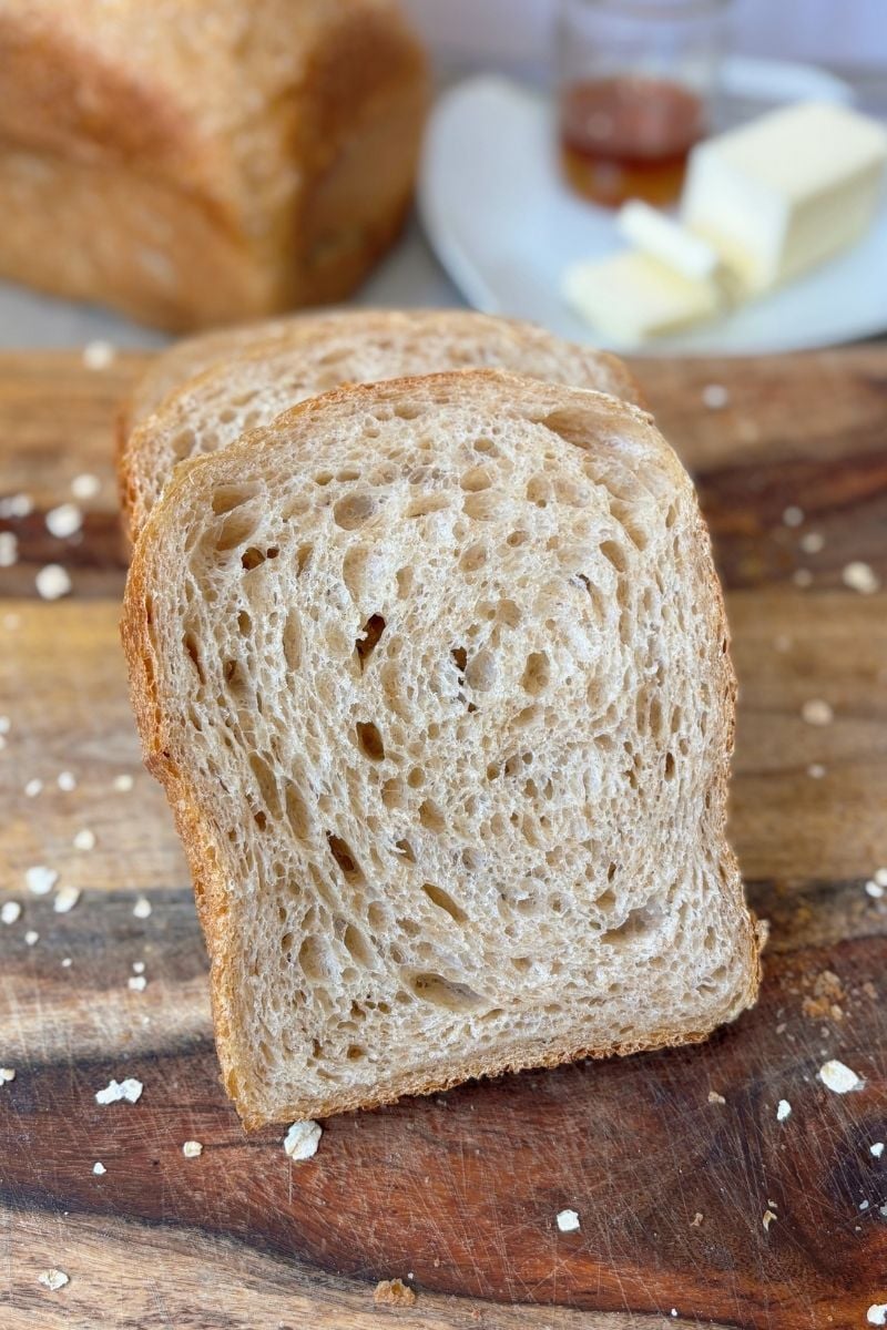 Honey Wheat Sourdough Sandwich Bread sliced on a wooden cutting board with butter and honey in the background