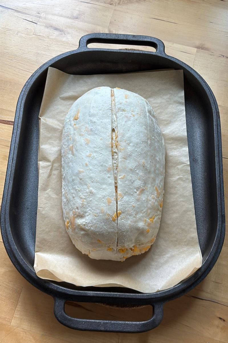scored Cheddar and Onion Sourdough dough on a piece of parchment paper in a challenger bread oven