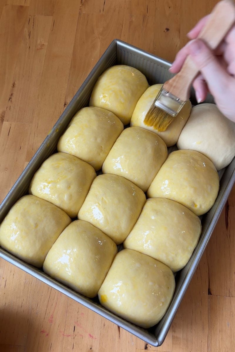 Brushing egg wash on a pan of rolls 